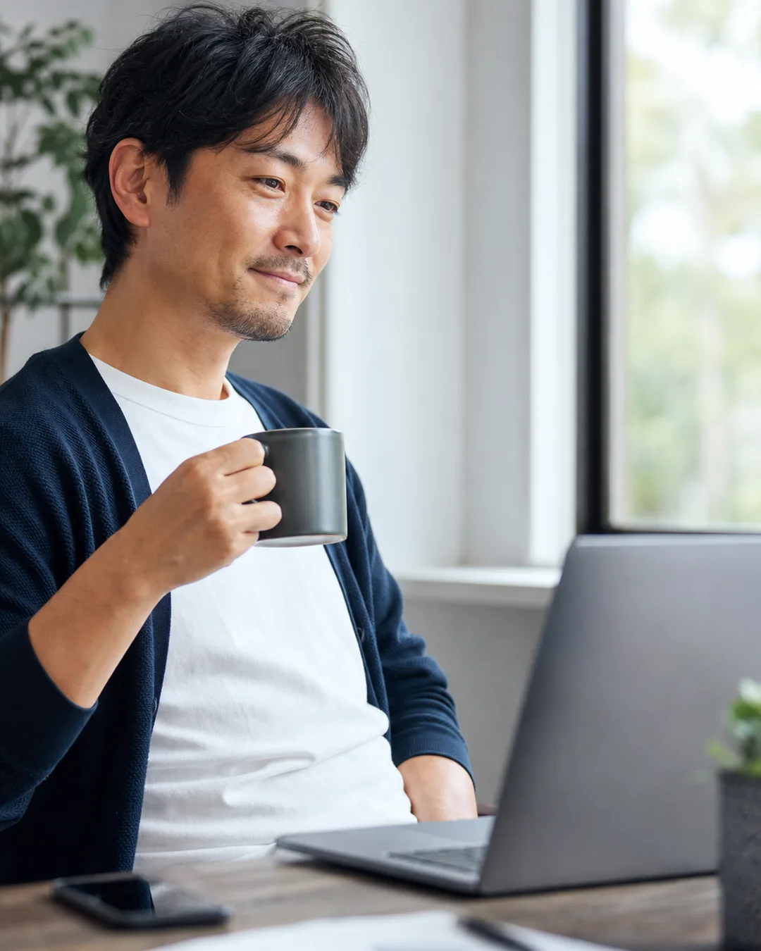 朝の明るいデスクでコーヒー片手にダッシュボードを確認する会社員